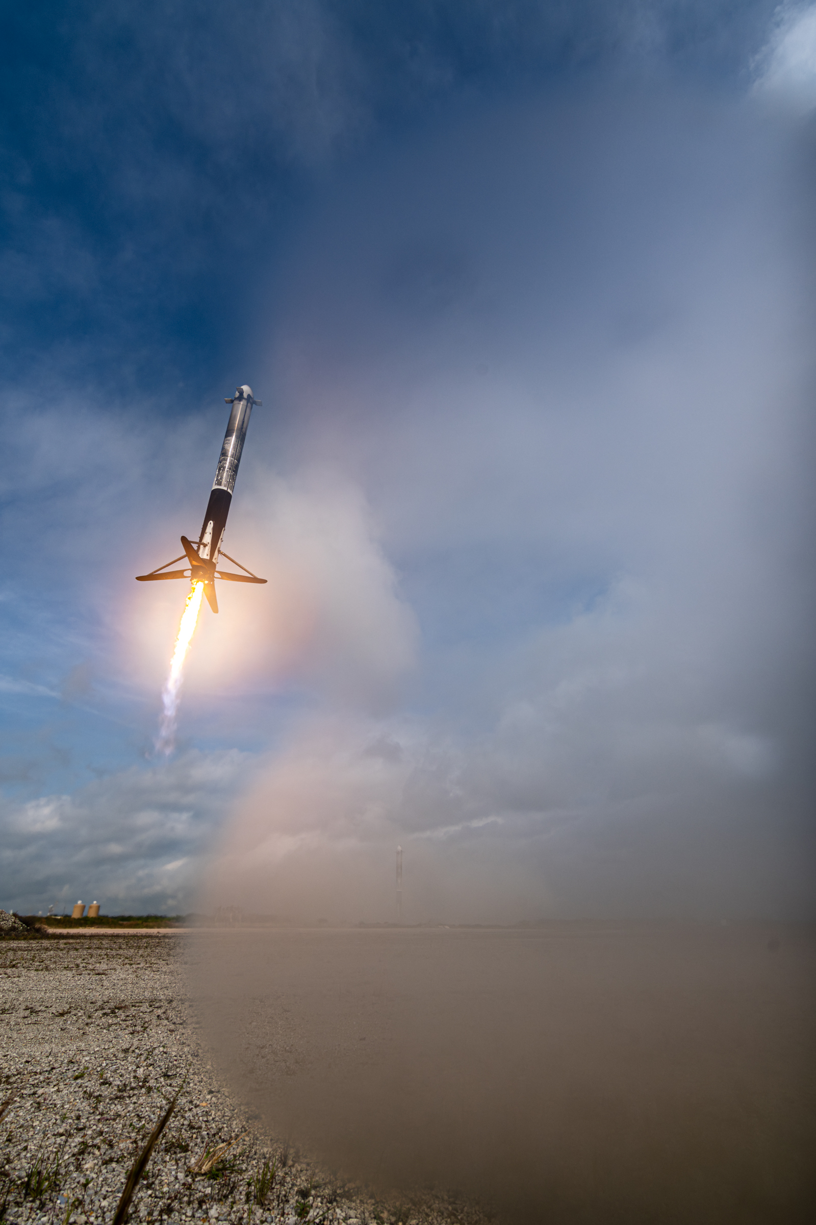 A side-core booster is coming in to land at LZ-1. The lens is wet from rain.